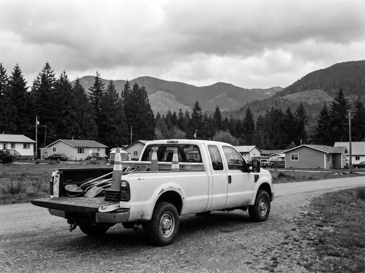 A work truck parked on a gravel road at the edge of a rural community